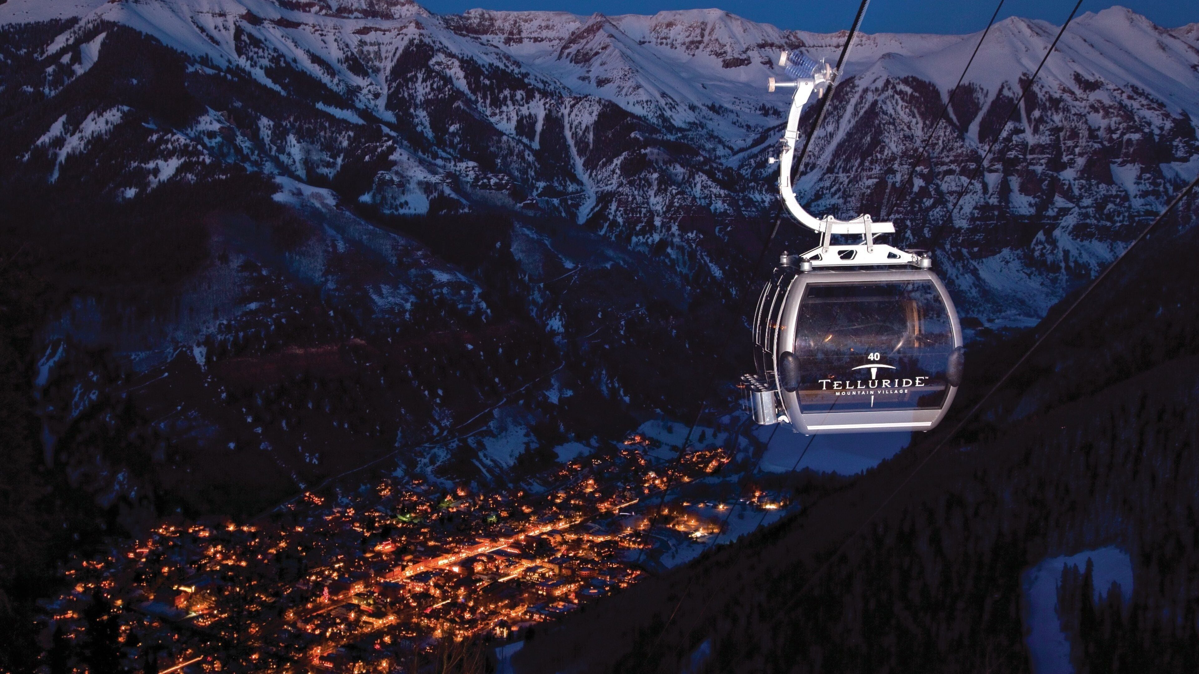 A cable car with 'Telluride Mountain Village' written on it, traveling over snow-covered mountains.