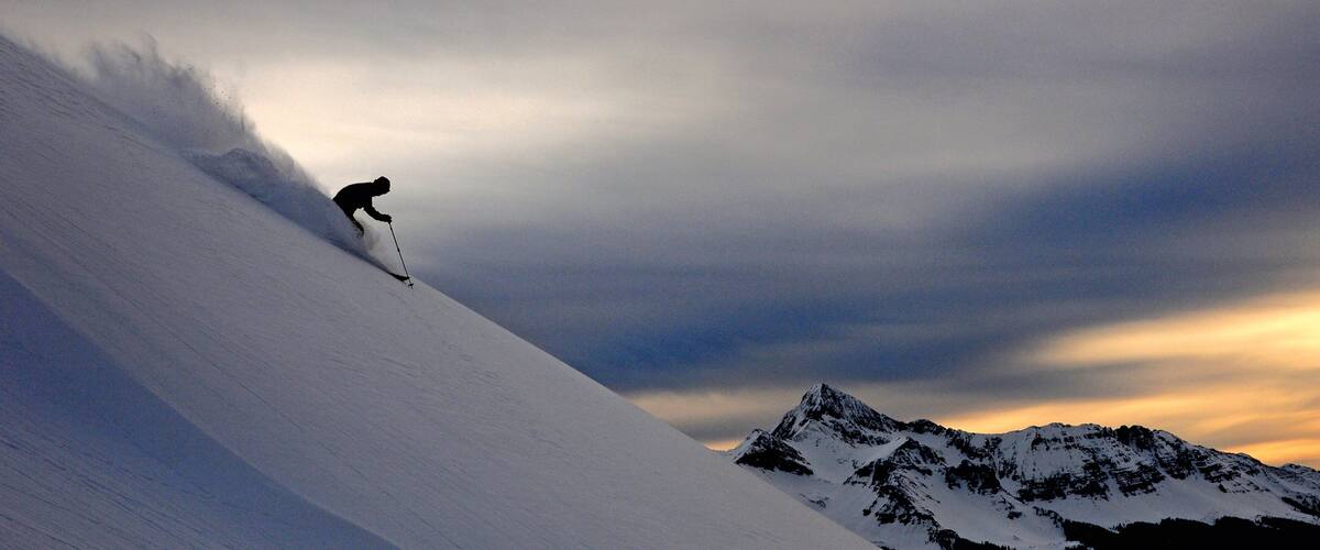 A skier on a snow-covered slope with a mountain range in the background.