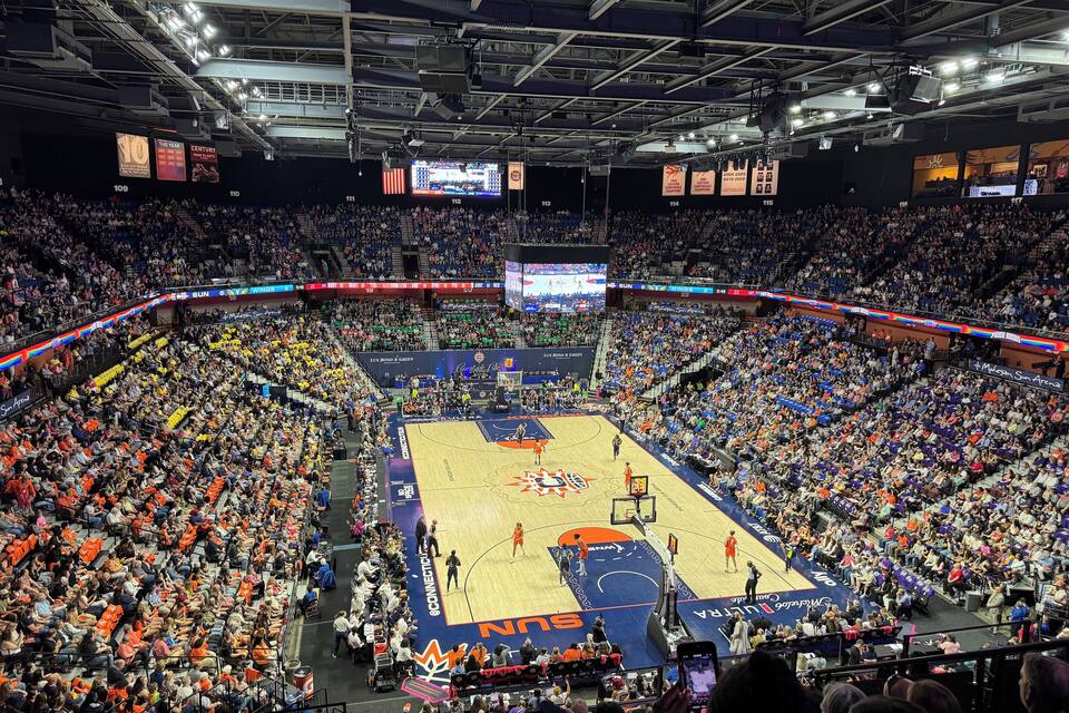 A basketball arena filled with spectators, a basketball court, and a large scoreboard.