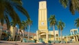 A tall clock tower with a statue at its base, surrounded by palm trees and a clear blue sky.