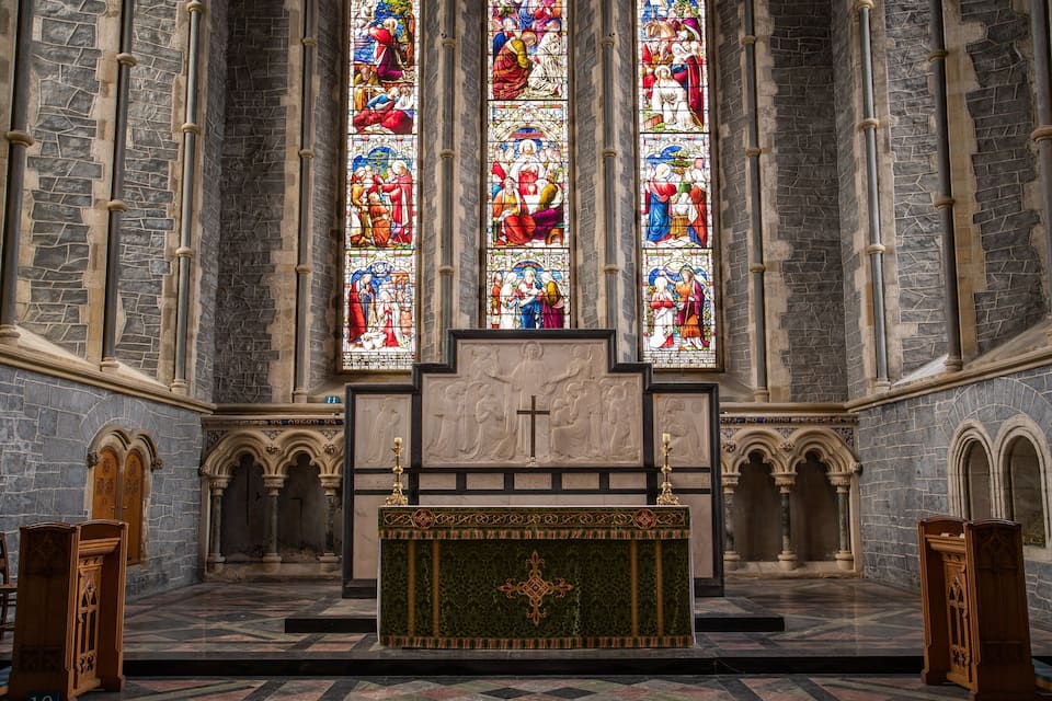 A church interior with stained glass windows, stone walls, and wooden pews.