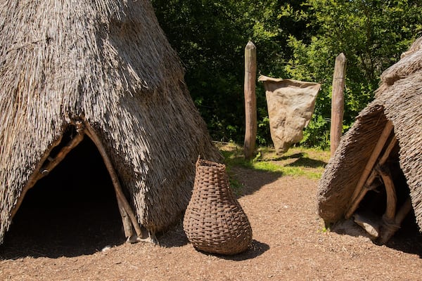 Des huttes aux toits de chaume, ornées de paniers tressés, et une grande structure en pierre, le tout intégré dans un environnement naturel.