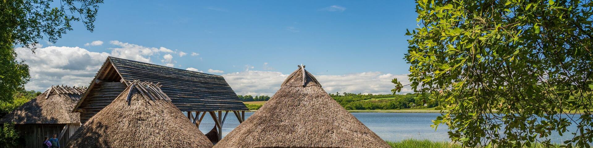 Thatched-roof huts by a lake, a wooden structure, and a clear blue sky.