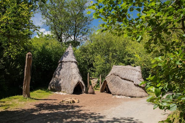 Une construction à toit de chaume, entourée d’arbres et de verdure.