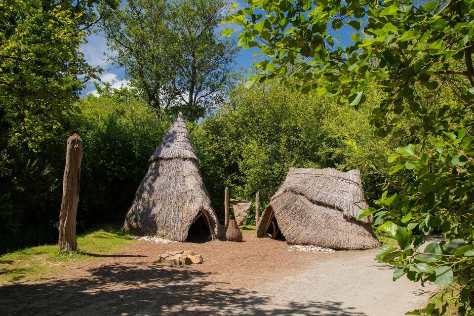 A thatched-roof structure surrounded by trees and greenery.