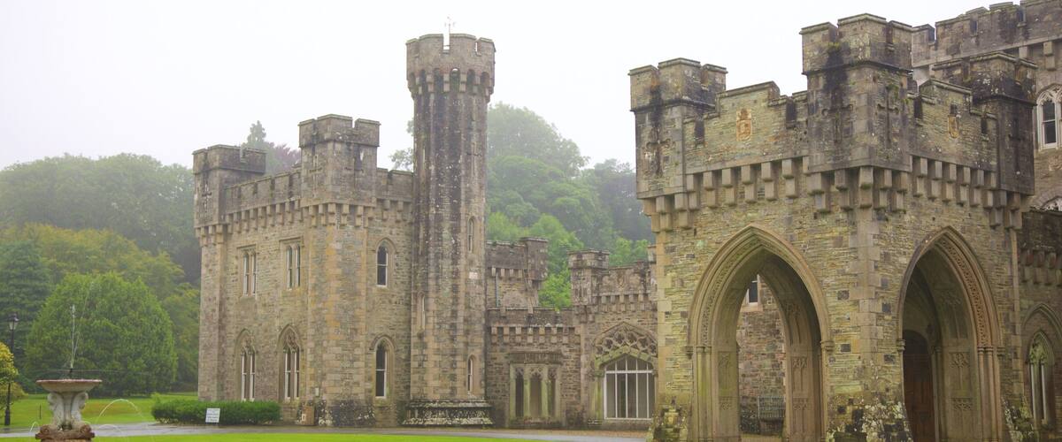 A historic castle with a large central tower, arched entrance, and surrounding lush greenery.