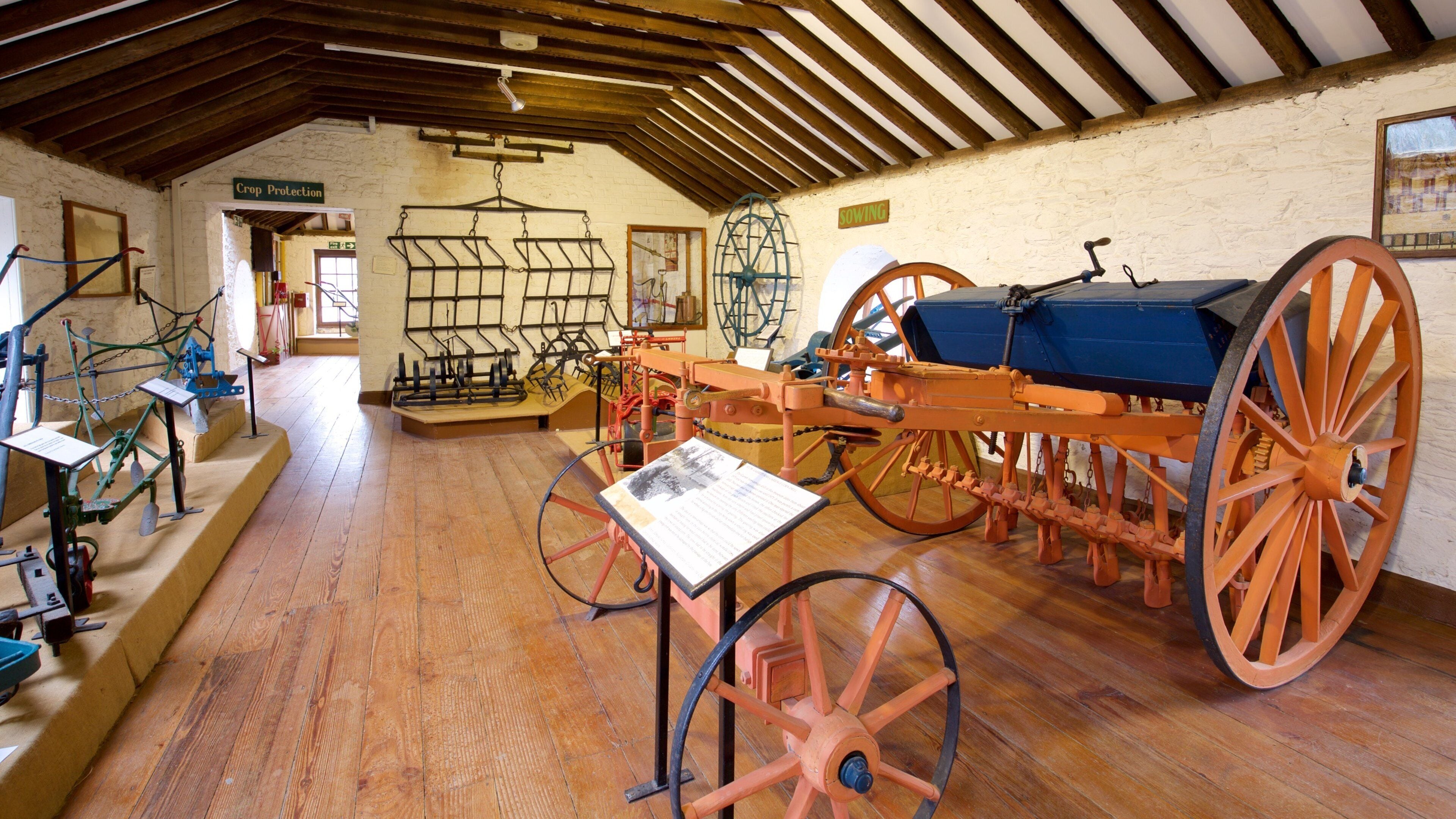 A museum exhibit with agricultural machinery, including a large orange plow and various farming tools.