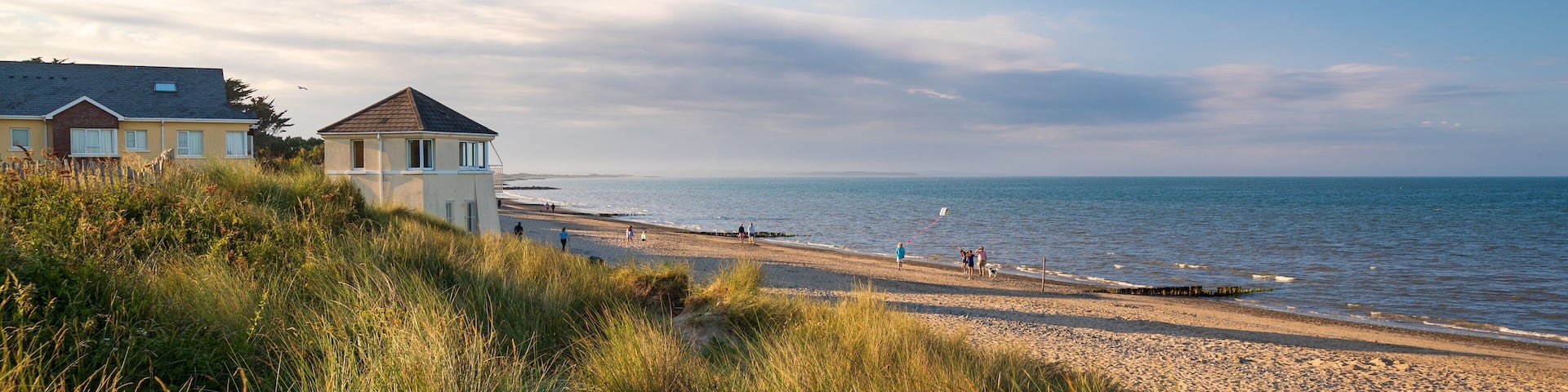 A coastal landscape with a beach, grassy dunes, and houses near the water.