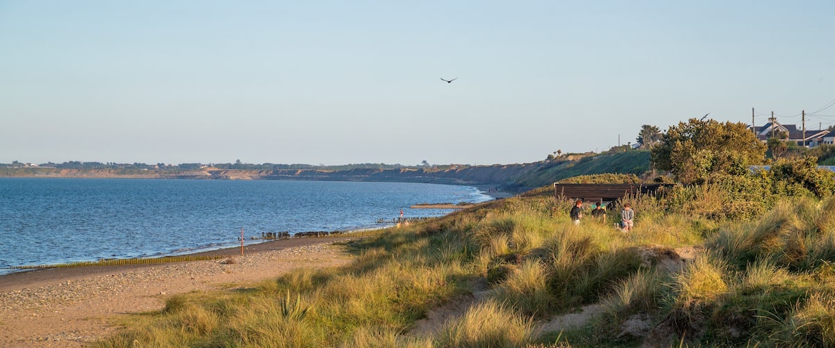 A coastal landscape with a sandy beach, grassy dunes, and a clear view of the sea.