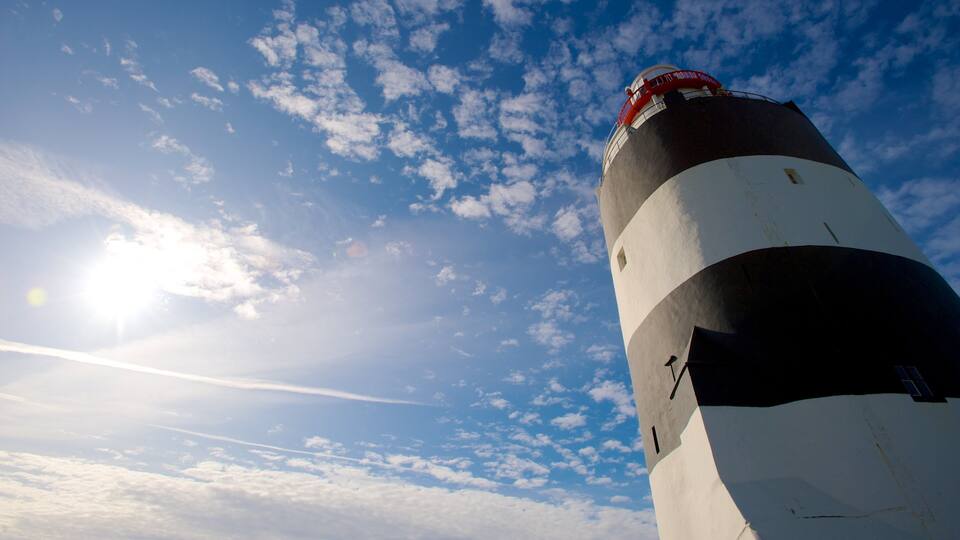 A lighthouse with a red top, set against a partly cloudy sky.