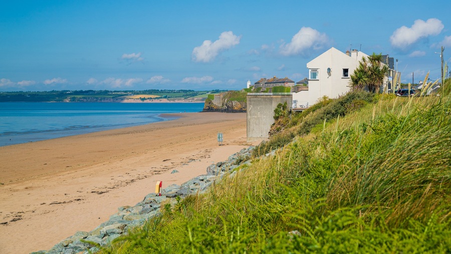 A sandy beach with a white house and a lighthouse in the background.