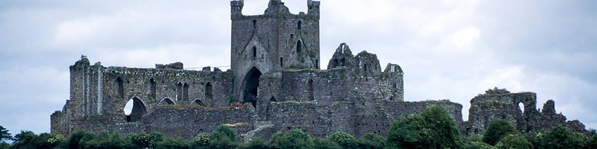 A historic castle with ruins, surrounded by a grassy field and a body of water.