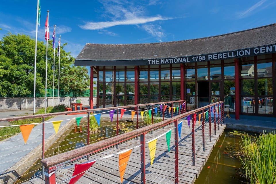 The National 1798 Rebellion Centre with a wooden bridge and colorful flags.