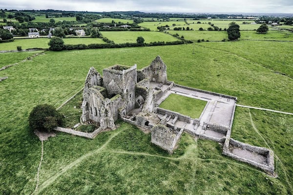 Vista aérea de uma ruína de castelo histórico cercada por campos verdes exuberantes.