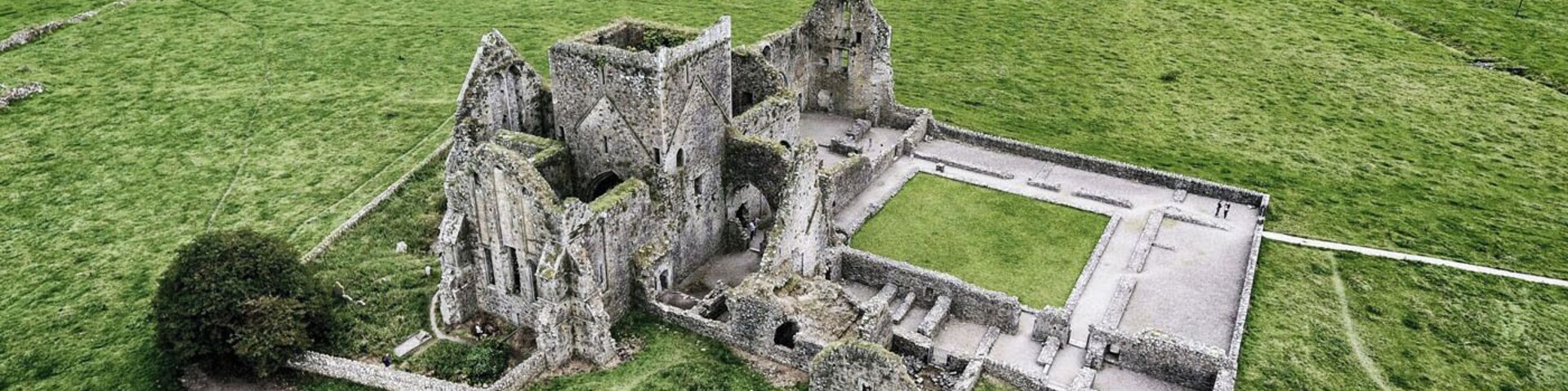 Vista aérea de uma ruína de castelo histórico cercada por campos verdes exuberantes.
