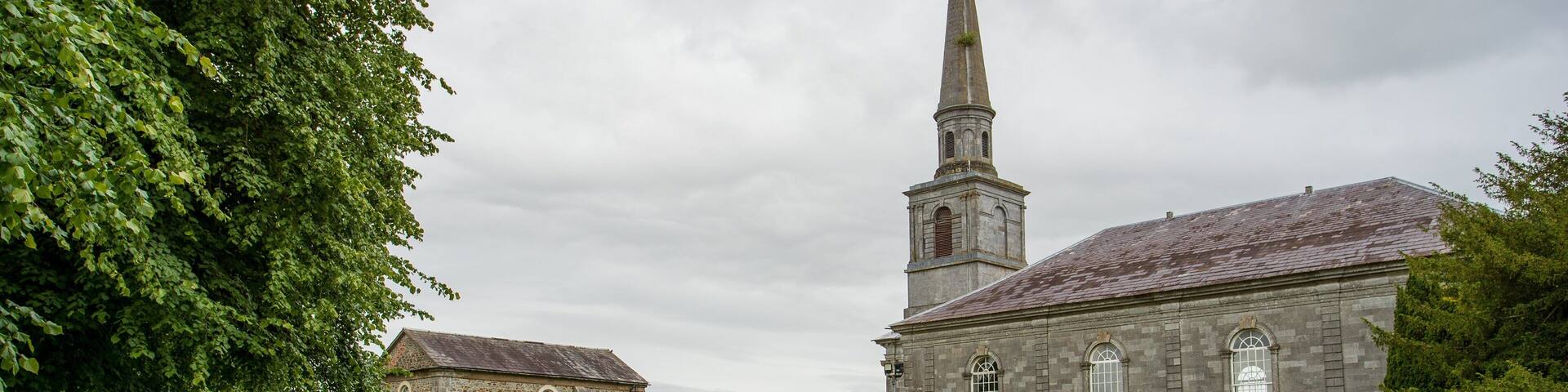 A church with a tall steeple and a graveyard in front.