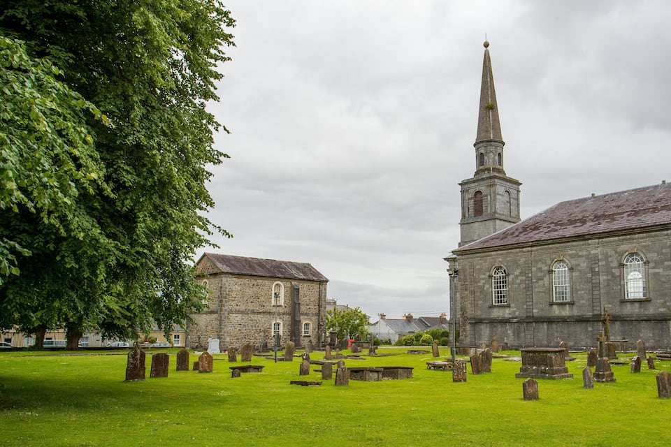 A church with a tall steeple and a graveyard in front.