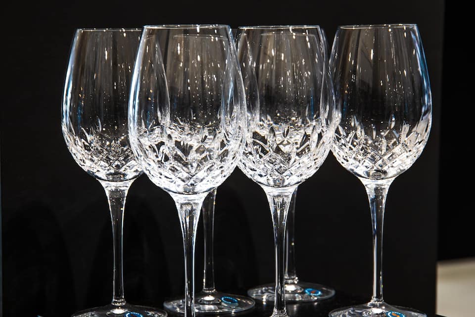 Cuatro copas de cristal con elaborados diseños grabados, sobre una superficie reflectante sobre fondo oscuro.