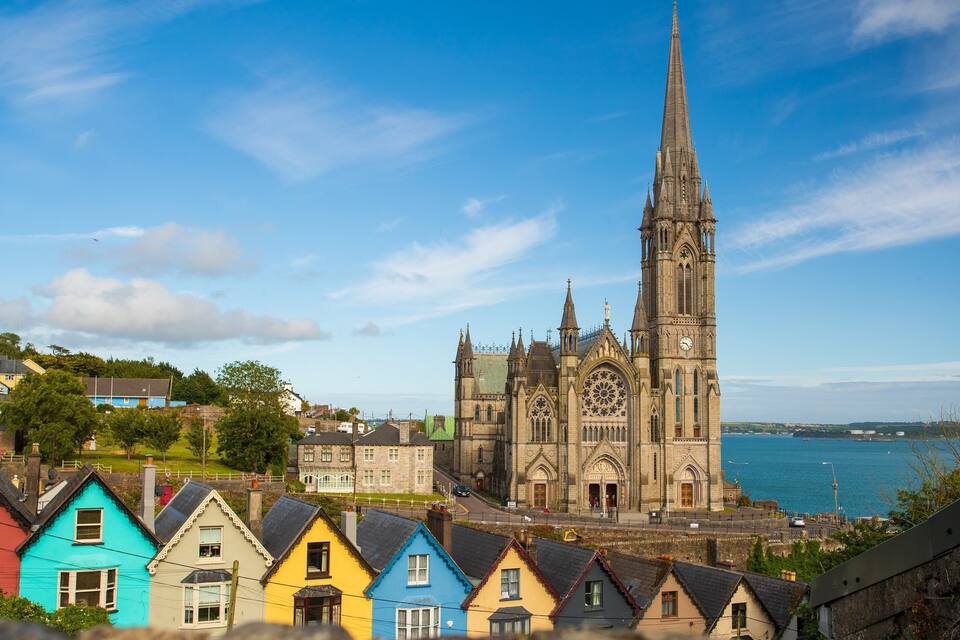 A coastal town with colorful houses, a prominent church with a tall spire, and a body of water in the background.