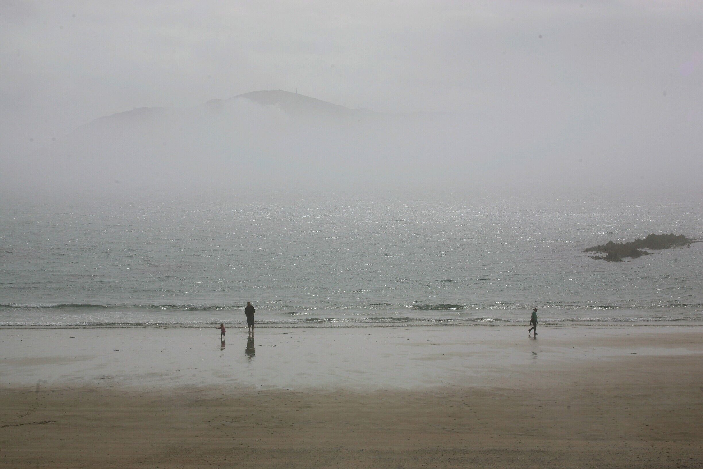 A foggy beach with a person standing and a child walking.