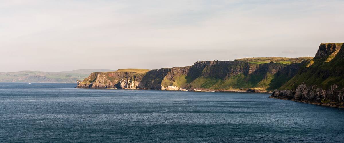 A coastal landscape with cliffs and a calm sea.