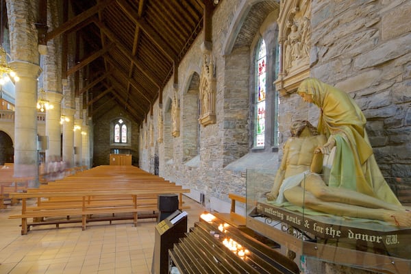 Ein Kircheninneres mit Holzbänken, Steinmauern und einer knienden Frauenstatue.