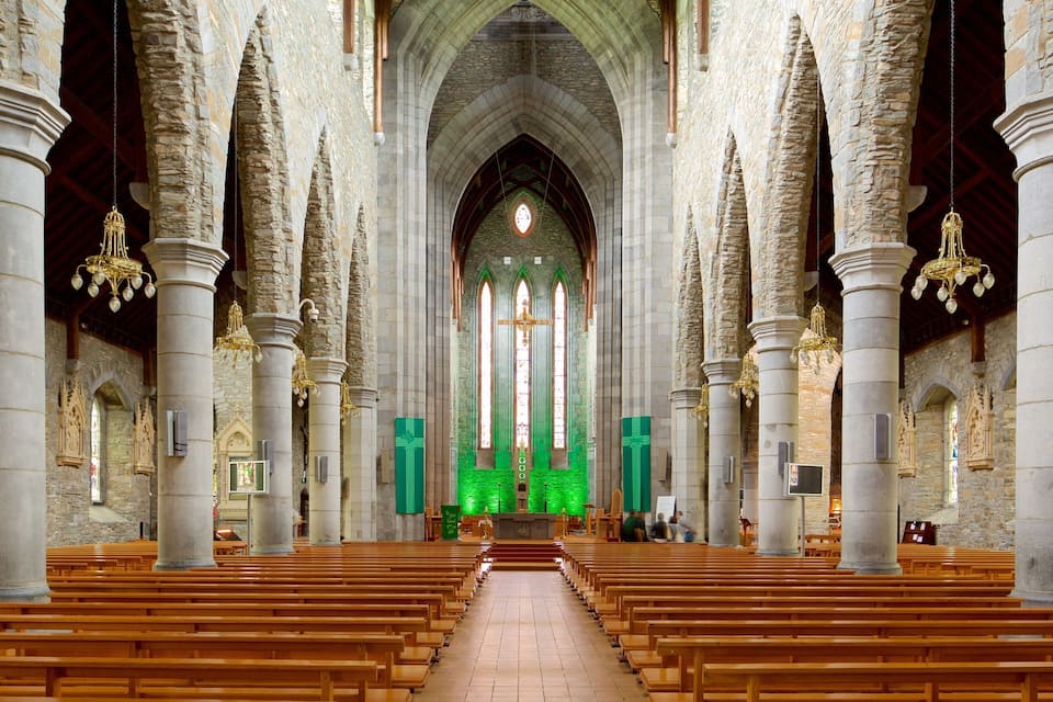 Interior de iglesia con columnas de piedra, bancos de madera y un altar iluminado en verde.
