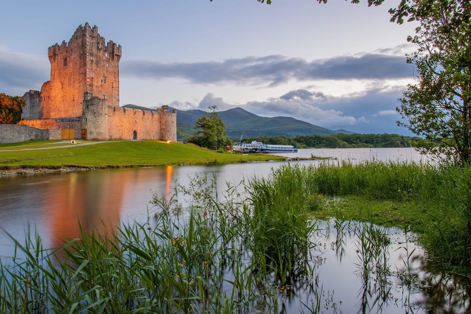Un castillo histórico junto a un lago tranquilo, con un bote al fondo.