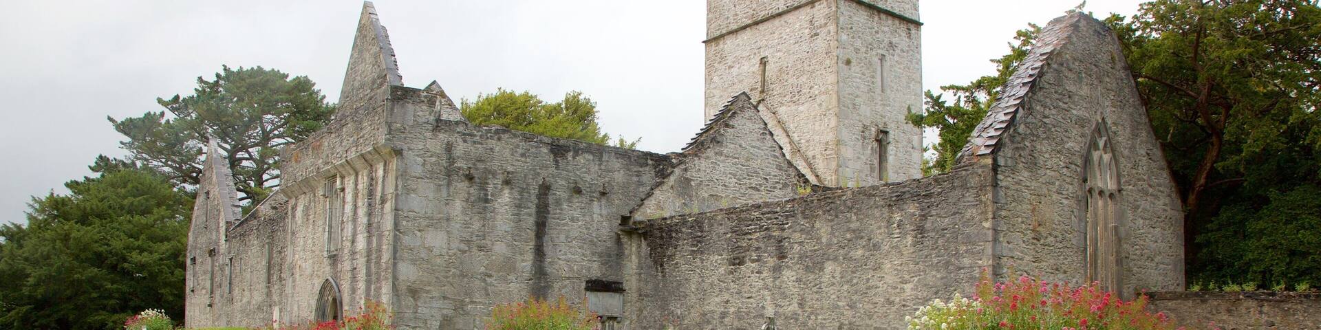 An old stone church with a tower and a graveyard with flowers.