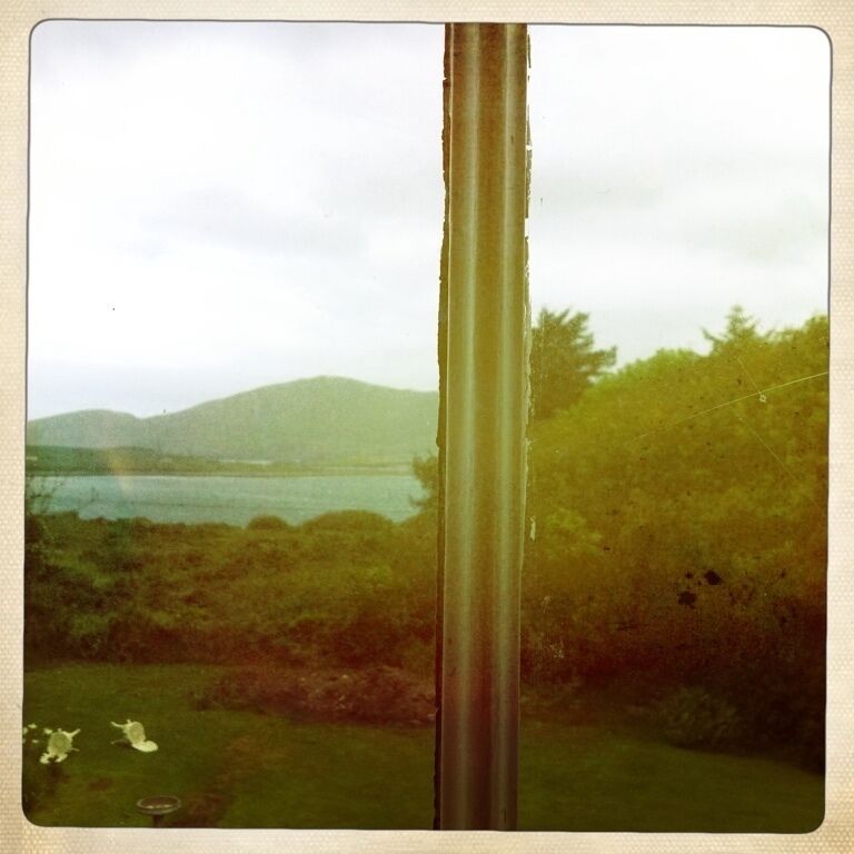 A view through a window with a metal pole, a grassy area, and distant hills.