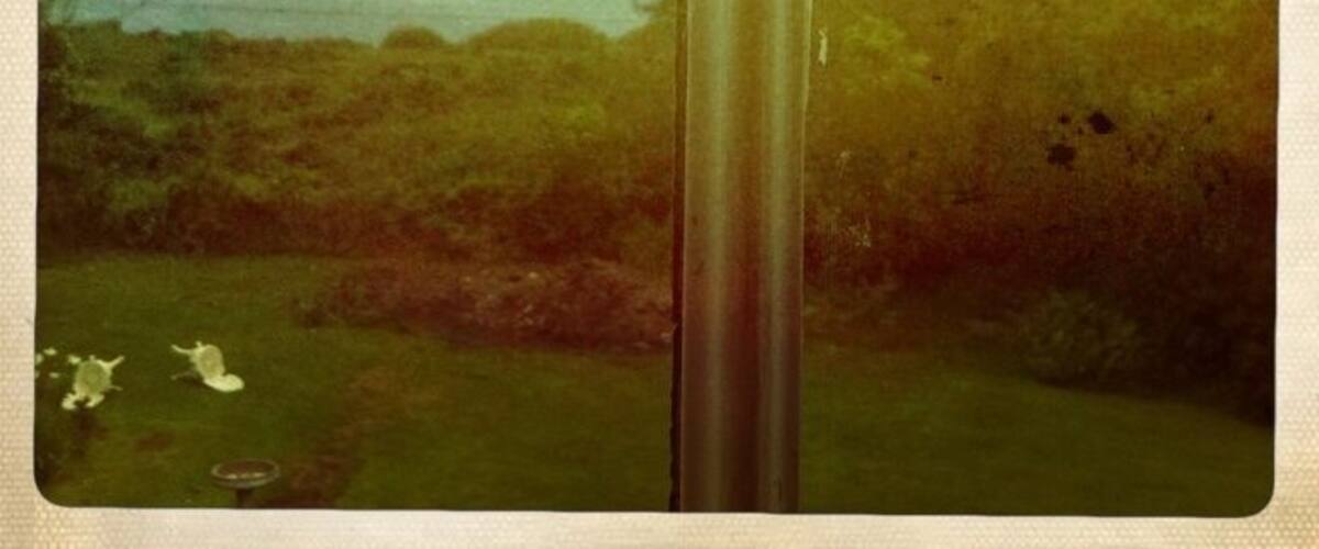 A view through a window with a metal pole, a grassy area, and distant hills.