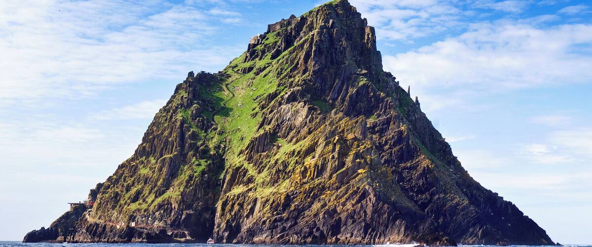 A rugged, green-clad mountain rising from the ocean, with a clear sky above.