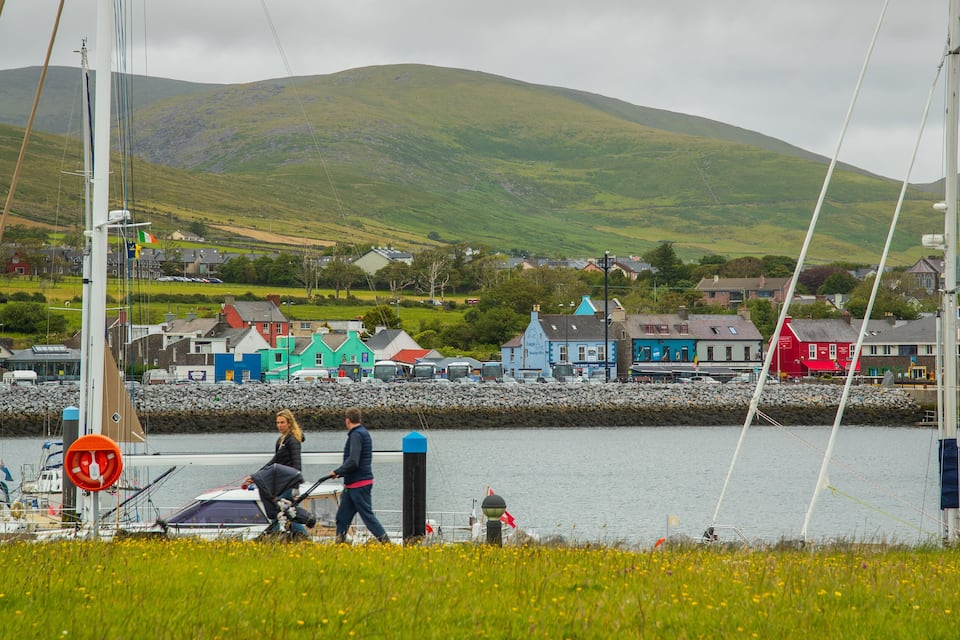 A harbor with boats, a rocky breakwater, and colorful buildings in the background.