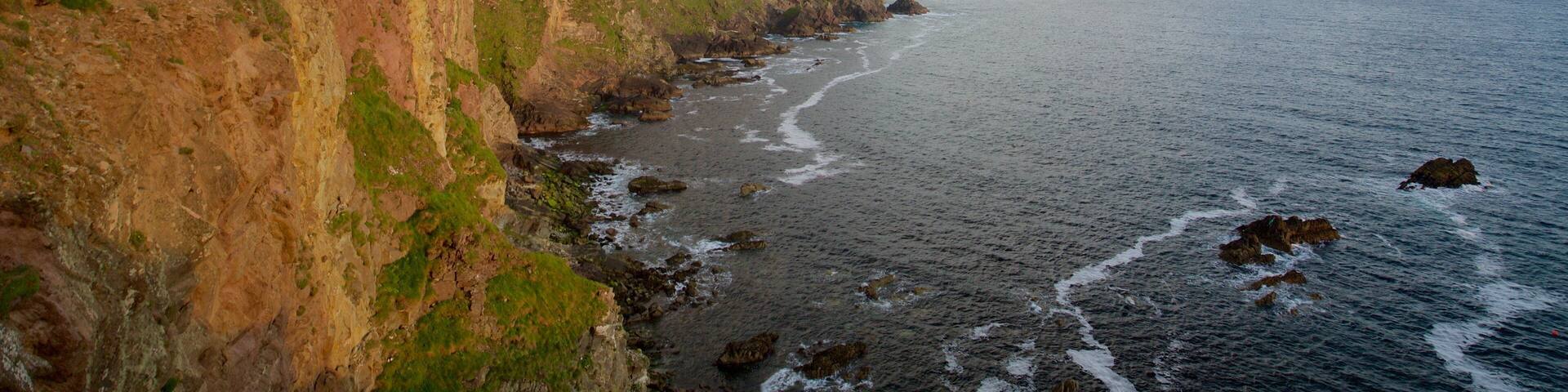 A coastal landscape with cliffs, a beach, and a distant hill.