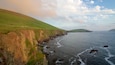 A coastal landscape with cliffs, a beach, and a distant hill.