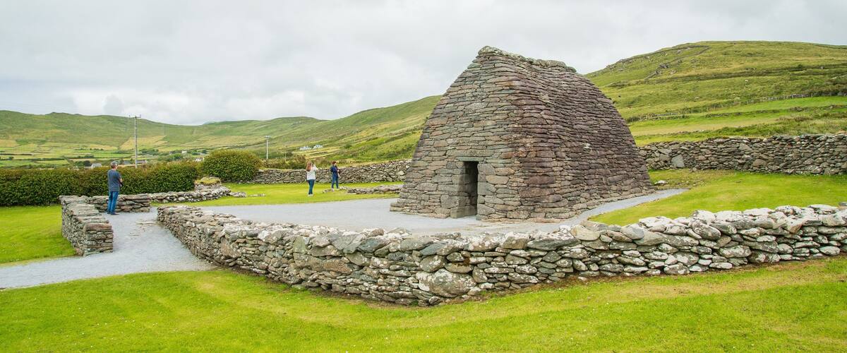 A stone structure with a triangular roof in a grassy field with hills in the background.