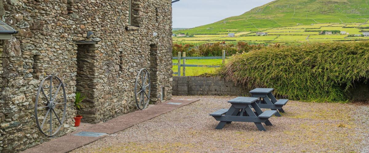 A stone building with a bicycle, picnic tables, and a green landscape in the background.