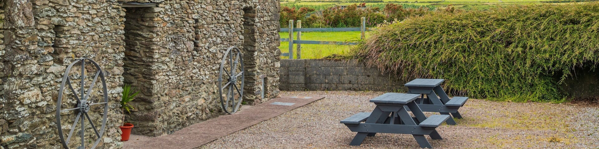A stone building with a bicycle, picnic tables, and a green landscape in the background.