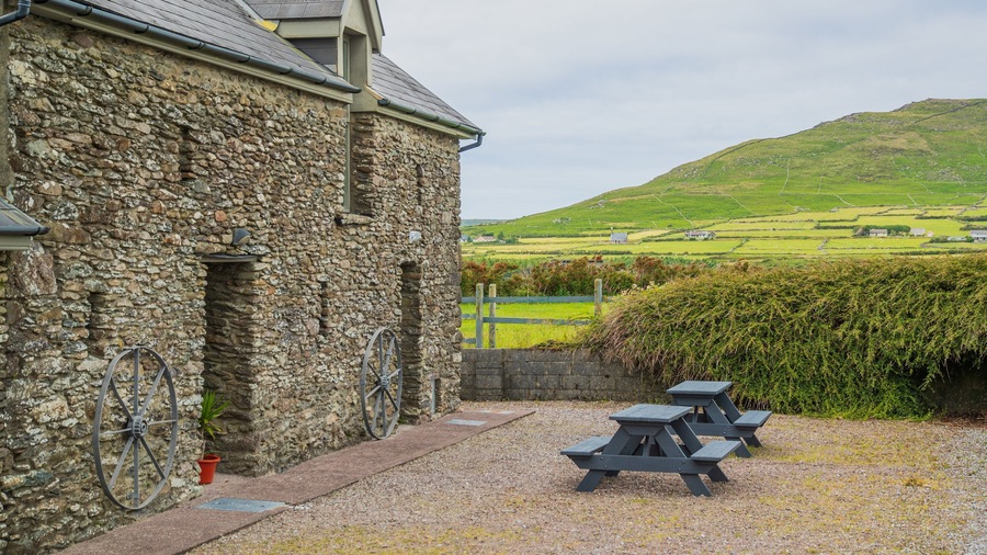 A stone building with a bicycle, picnic tables, and a green landscape in the background.