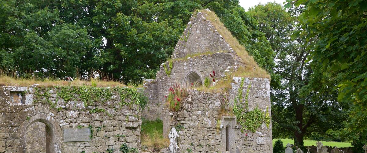 A stone structure with a triangular roof, surrounded by a cemetery with various headstones.
