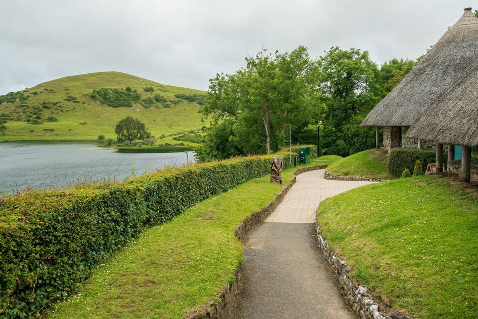 A thatched-roof house beside a lake with a pathway leading to it.