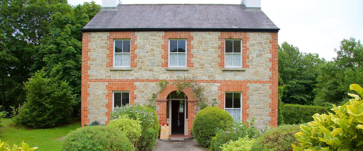 A stone house with a brick facade, a gravel driveway, and well-maintained gardens.