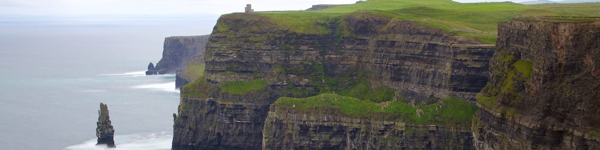 Eine Küstenklippe mit einem Leuchtturm und einem grasbewachsenen Hügel im Hintergrund.