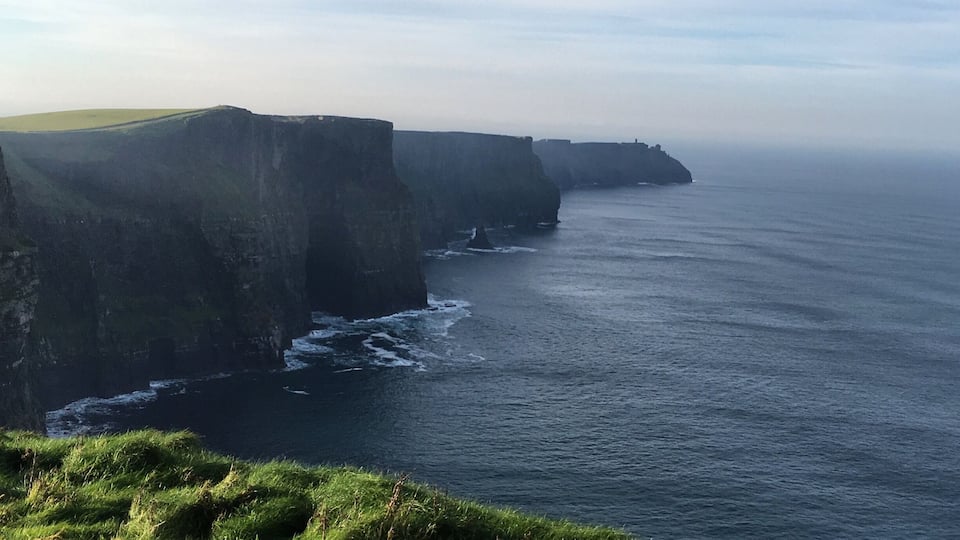 A coastal cliff with a grassy foreground and a view of the ocean.