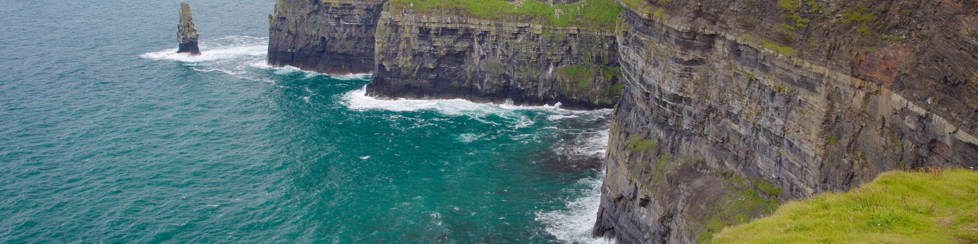 A coastal cliff with a lighthouse and grassy terrain.