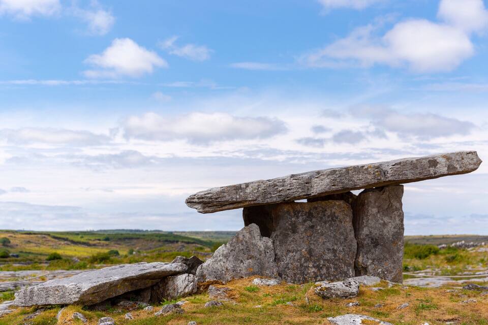 A standing stone structure in a grassy field with a cloudy sky.