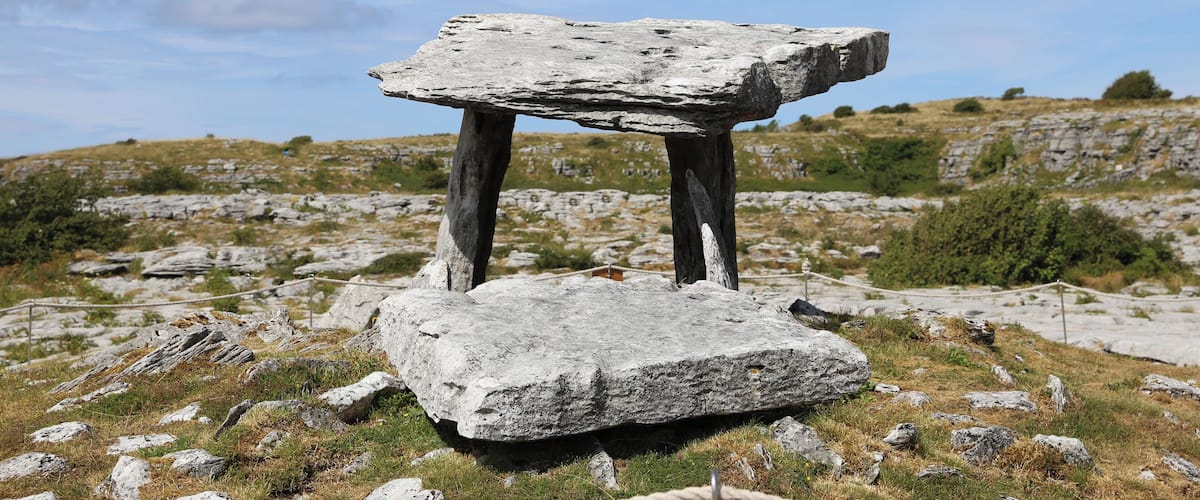 Una estructura de piedra vertical en un campo cubierto de hierba, con cielo despejado.