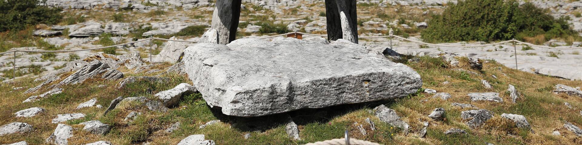 A standing stone structure in a grassy field with a clear sky.