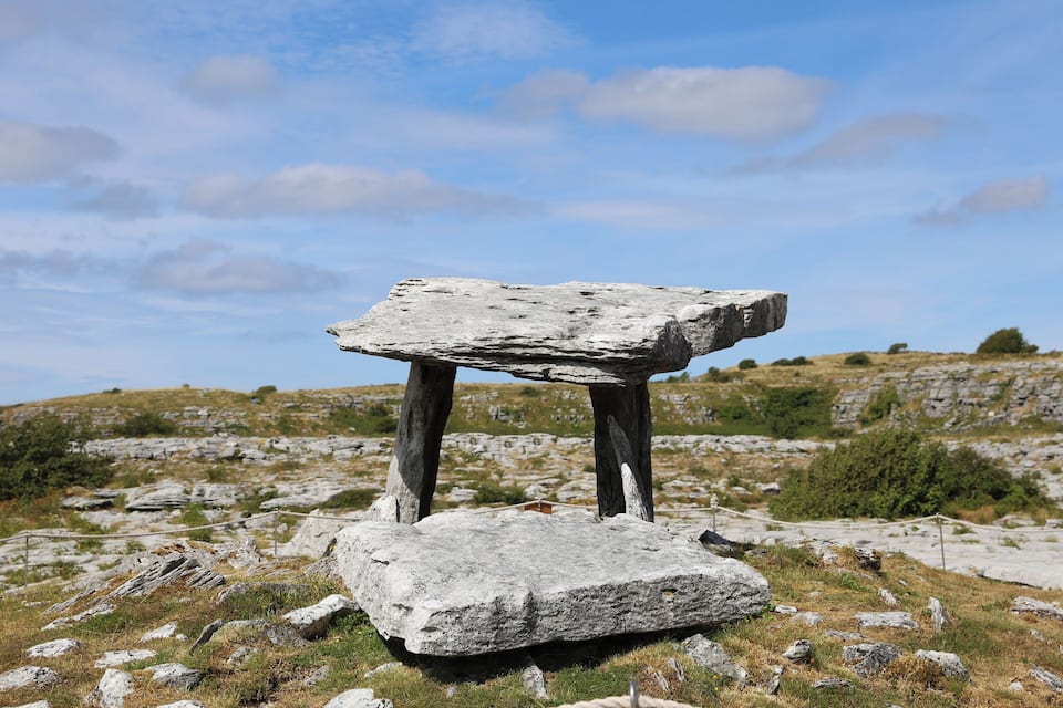 A standing stone structure in a grassy field with a clear sky.