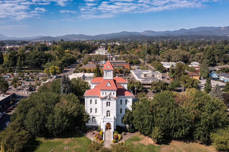 A large white building with a red roof and a clock tower, surrounded by trees and other buildings.